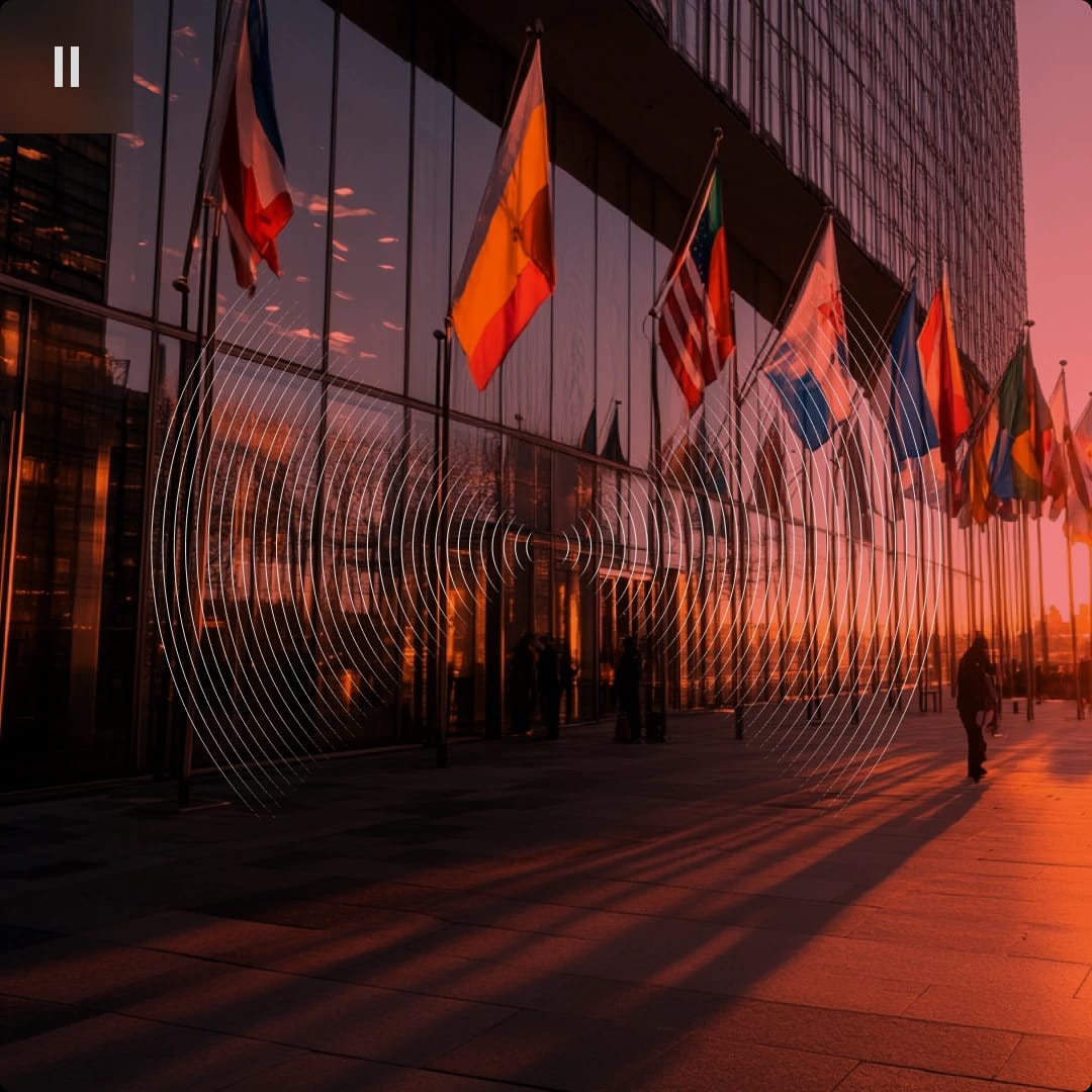 Flags of various countries outside a modern glass building at sunset.