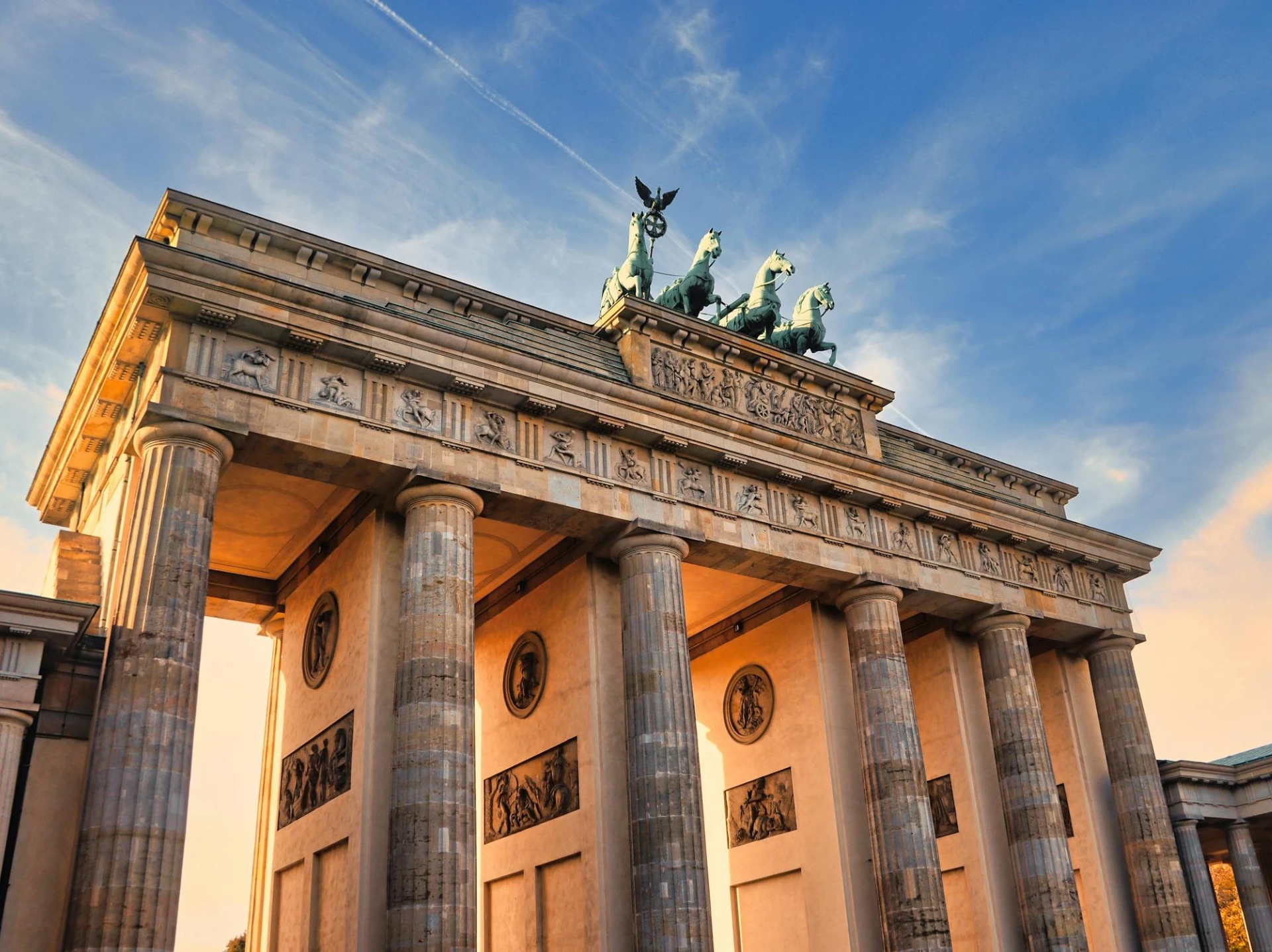 The Brandenburg Gate in Berlin, Germany, with a clear sky and the sun casting a warm glow on the structure.