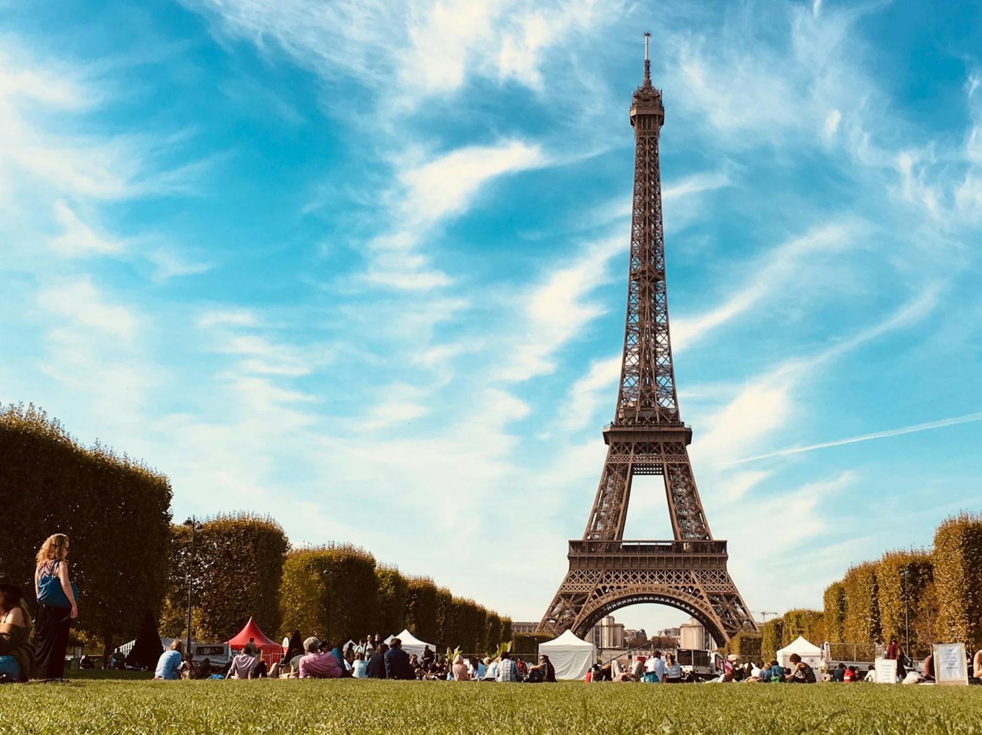People sitting and relaxing on the grass near the Eiffel Tower on a sunny day.