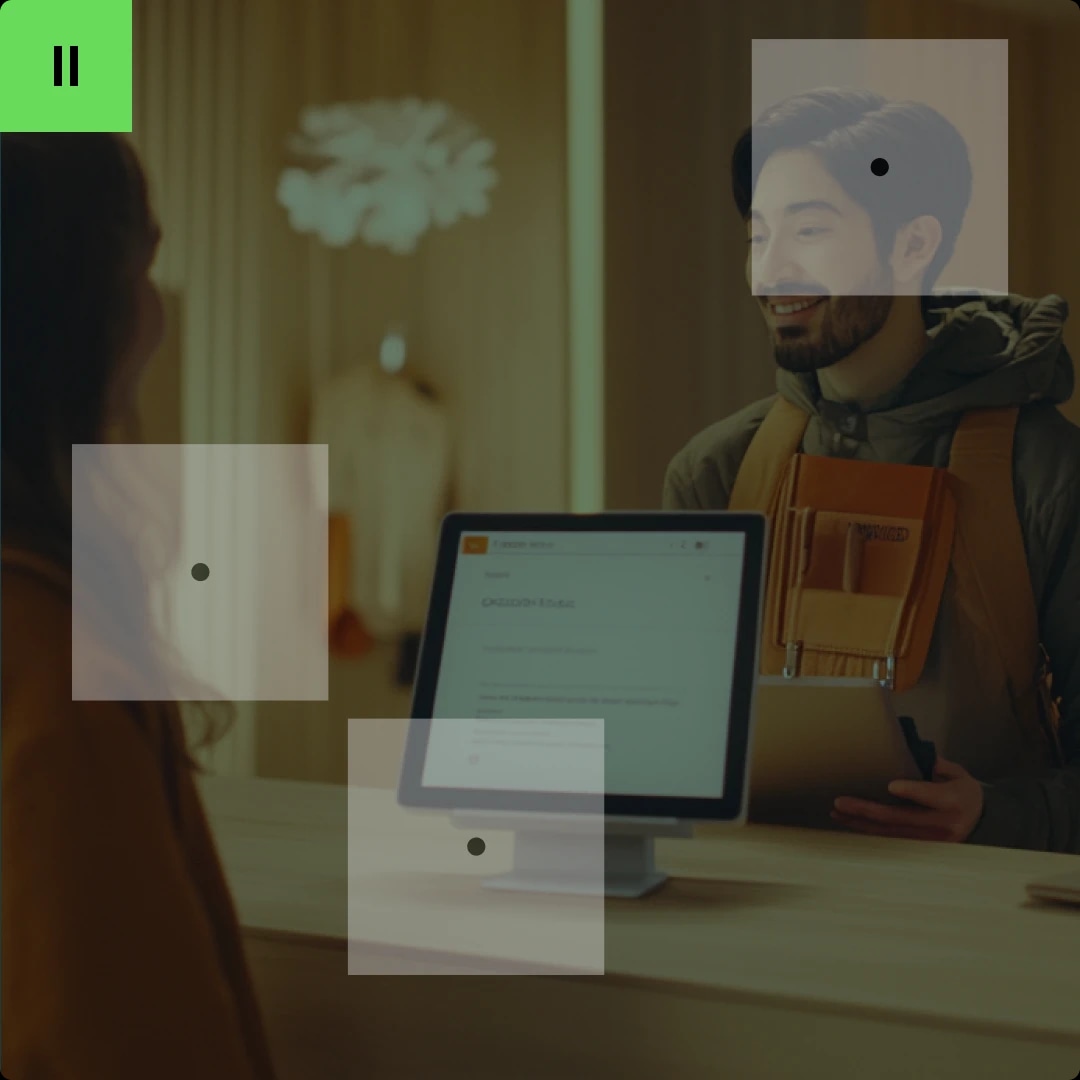 A man with a backpack talking to a woman at a reception desk with a computer monitor.