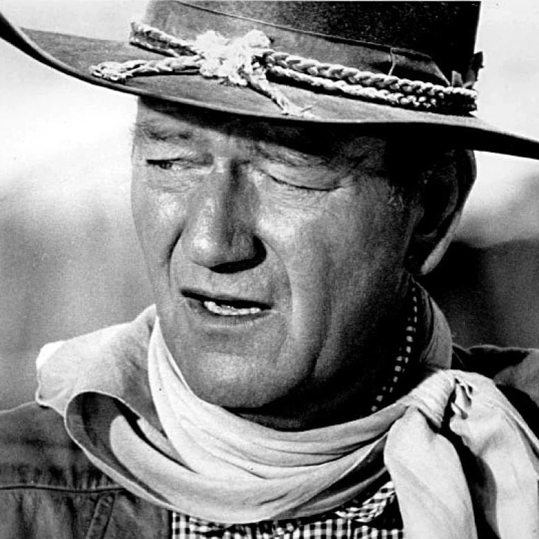 A man wearing a cowboy hat with a decorative band, squinting with a serious expression.