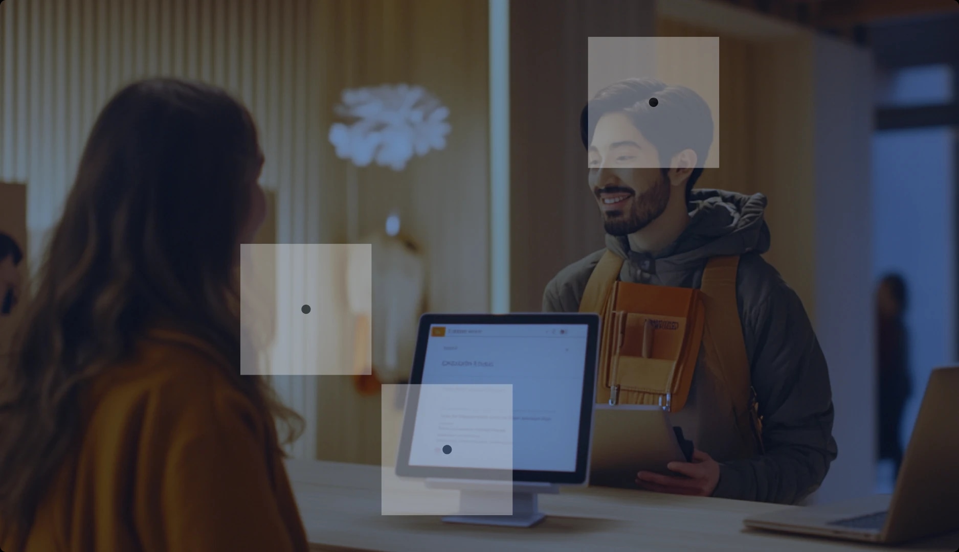 A man with a beard smiling at a woman at a reception desk, with a computer monitor in front of her.