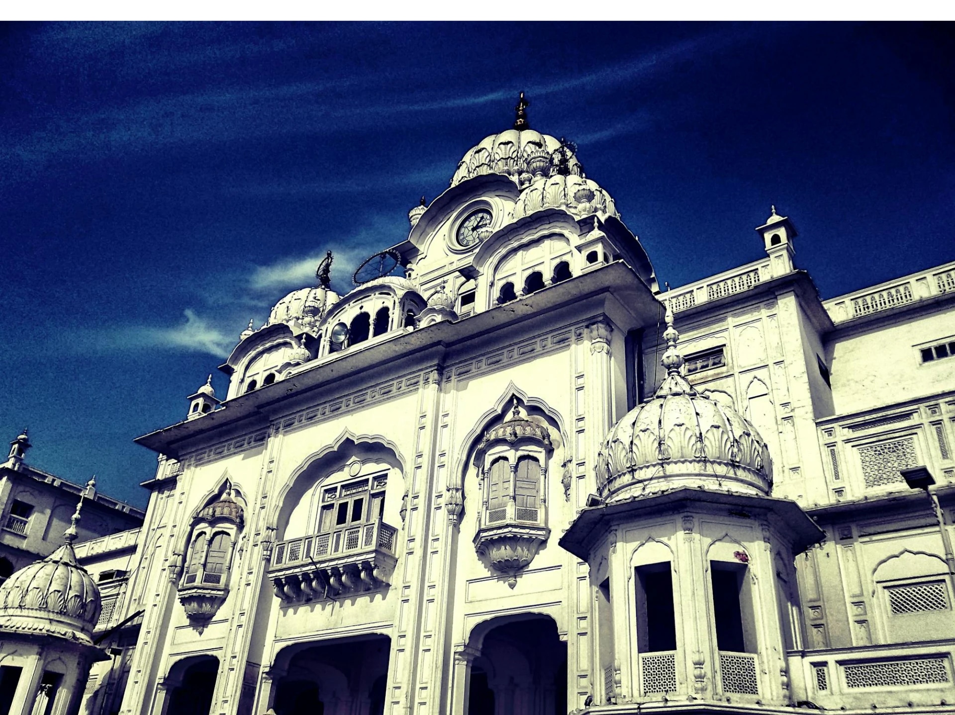 White historic building with domes and intricate architectural details against a blue sky.