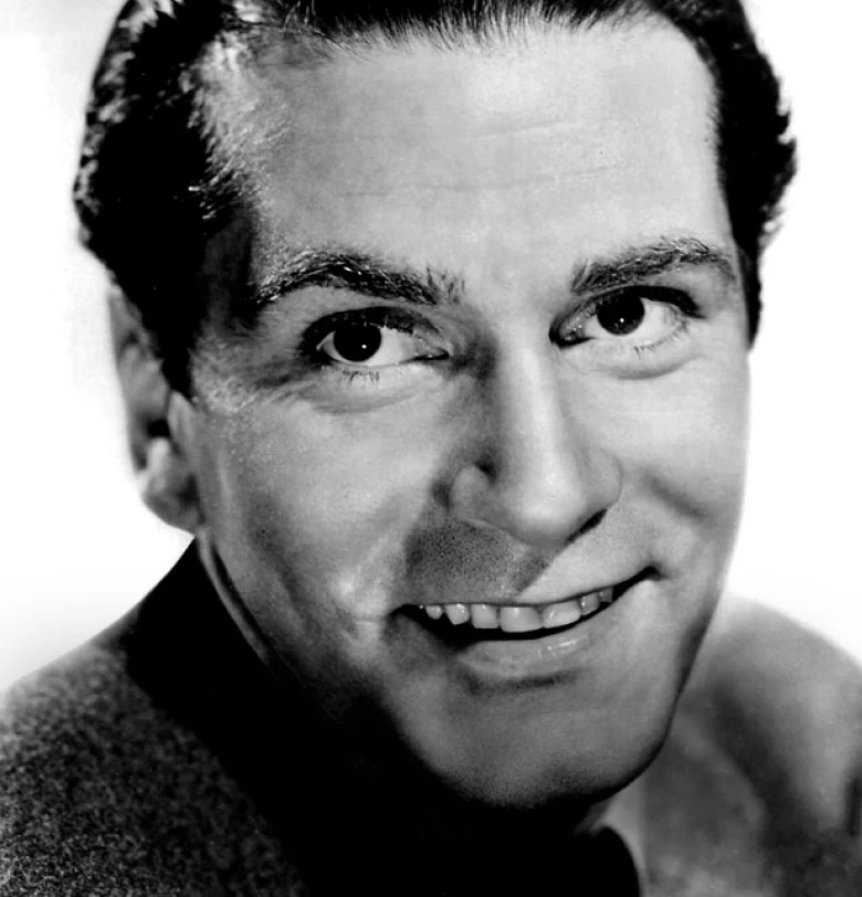 A black-and-white close-up portrait of a smiling man with dark hair and bright eyes.