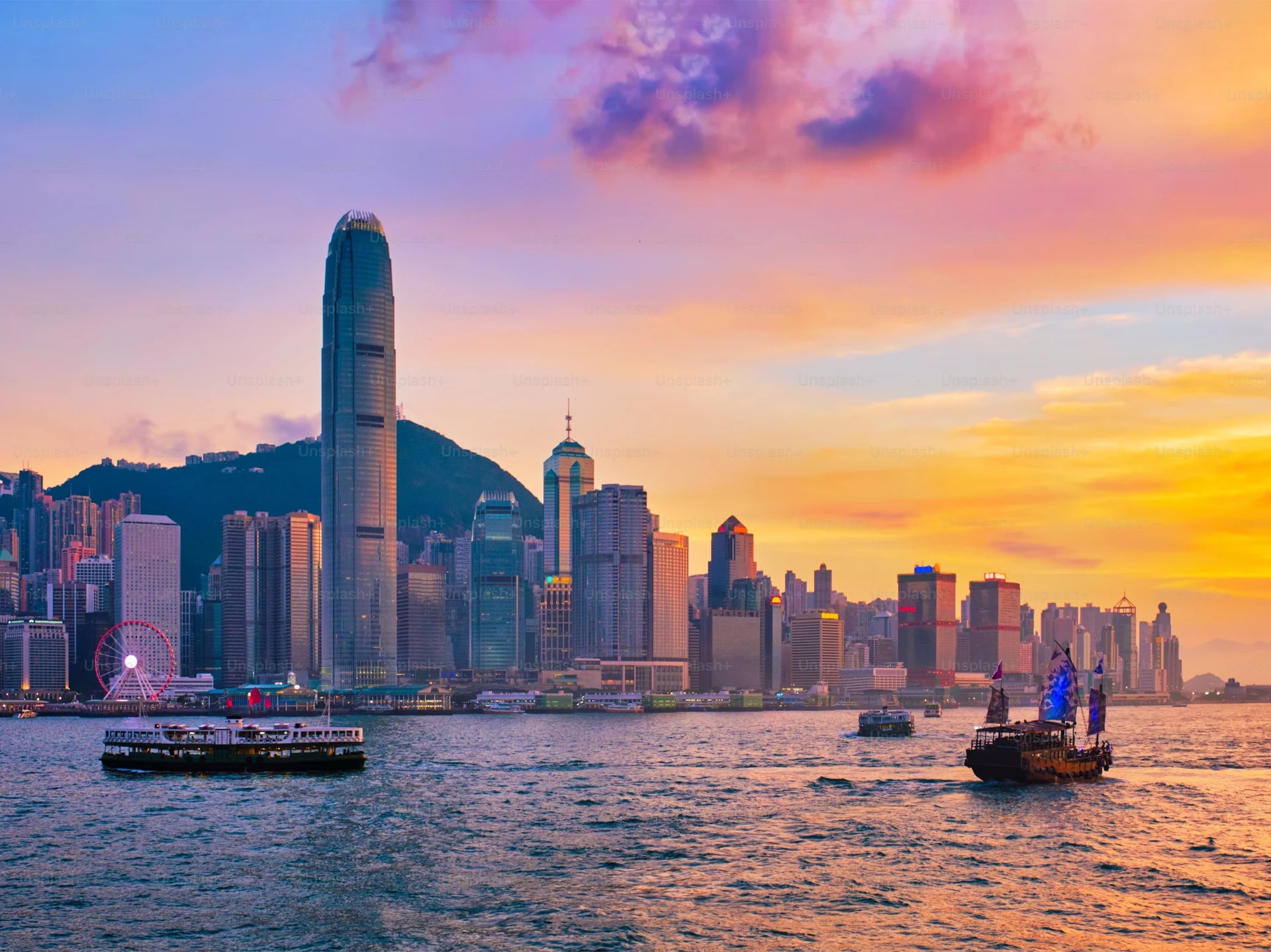 Hong Kong skyline at sunset with boats on Victoria Harbour.