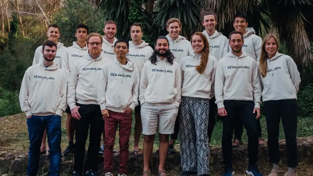 Group of people wearing white hoodies with "Eleven Labs" logo, standing outdoors in front of trees.