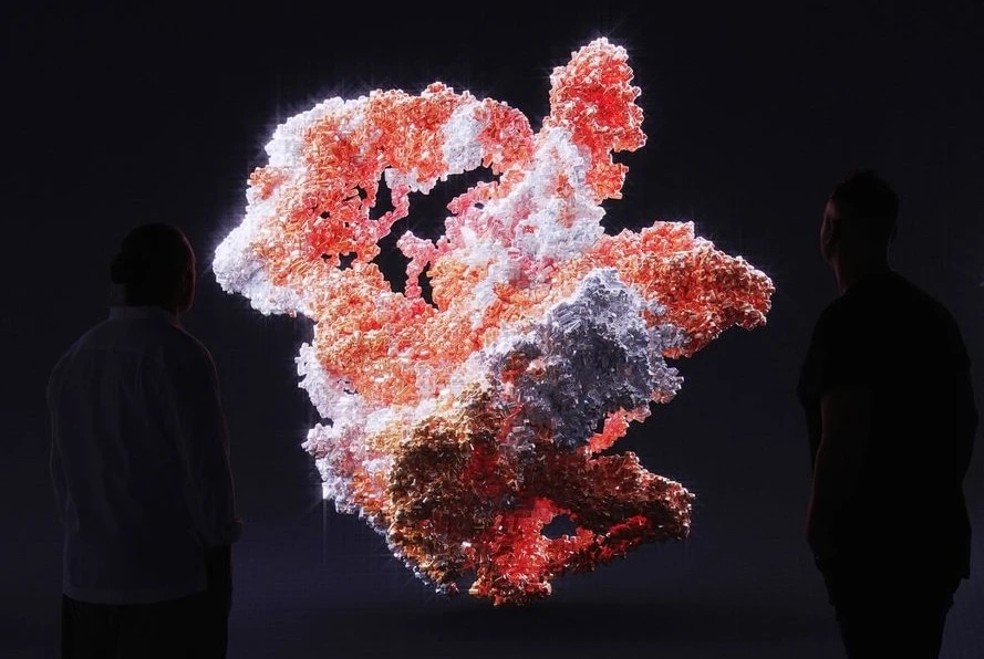 A digital art installation resembling a fragmented, glowing map of South America with two people observing it in a dark room.