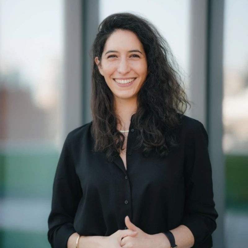 Tanner smiles with her hands crossed in front of her body. She is wearing a black shirt and black watch. 