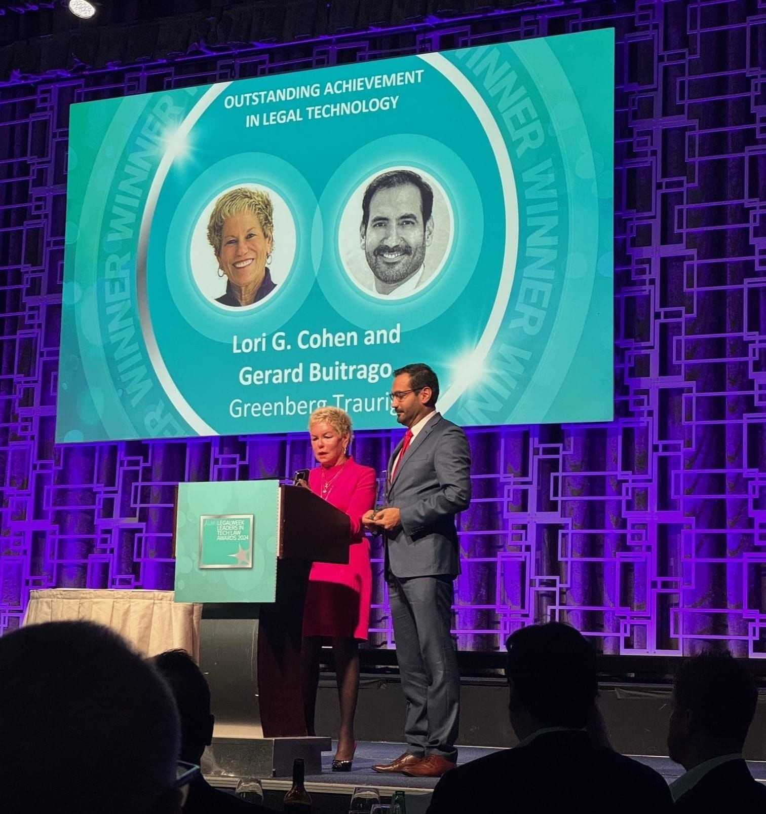 Lori G. Cohen and Gerard Buitrago accepting an award on stage at a conference.