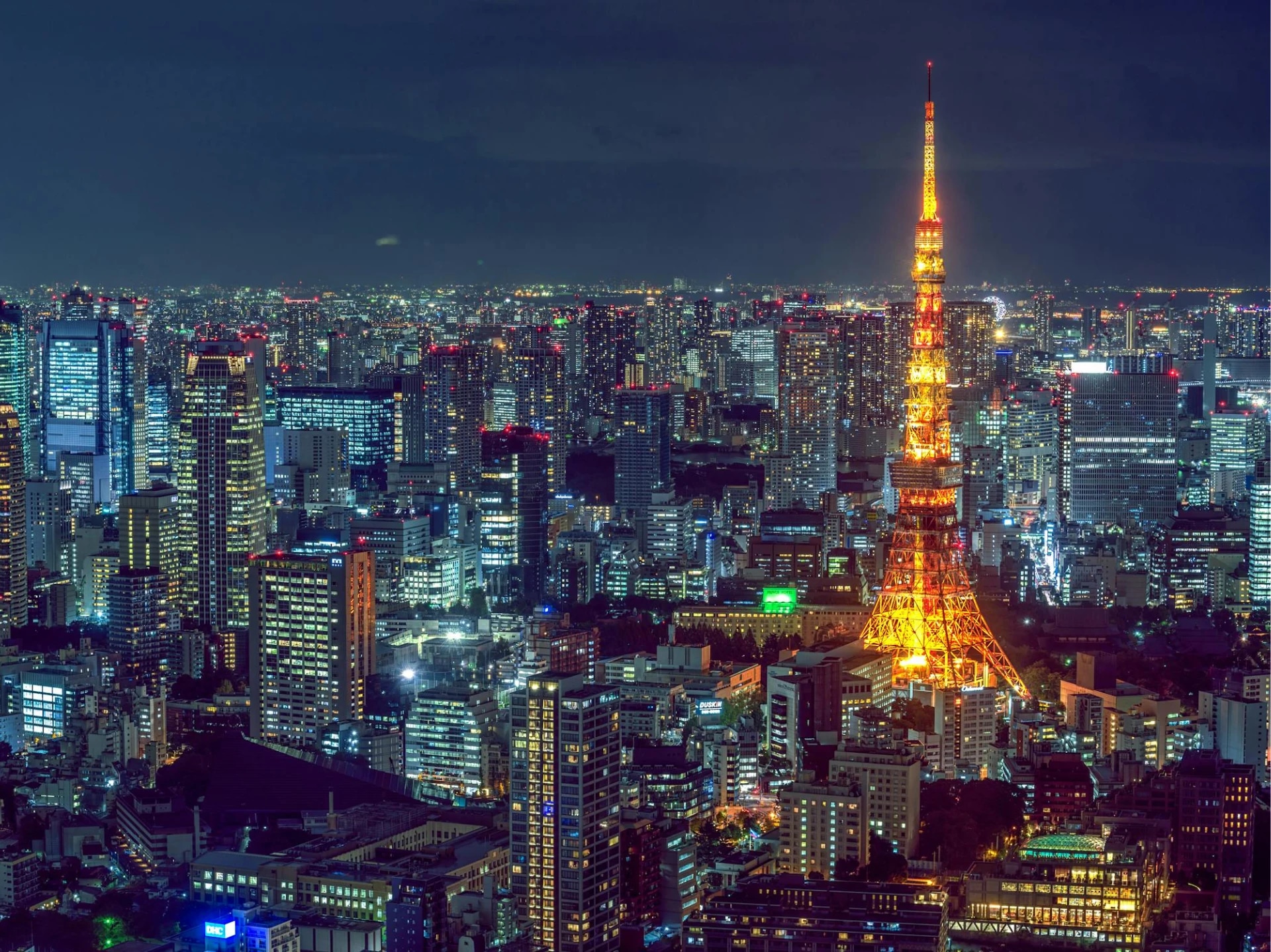 Tokyo Tower illuminated at night in a cityscape filled with skyscrapers.