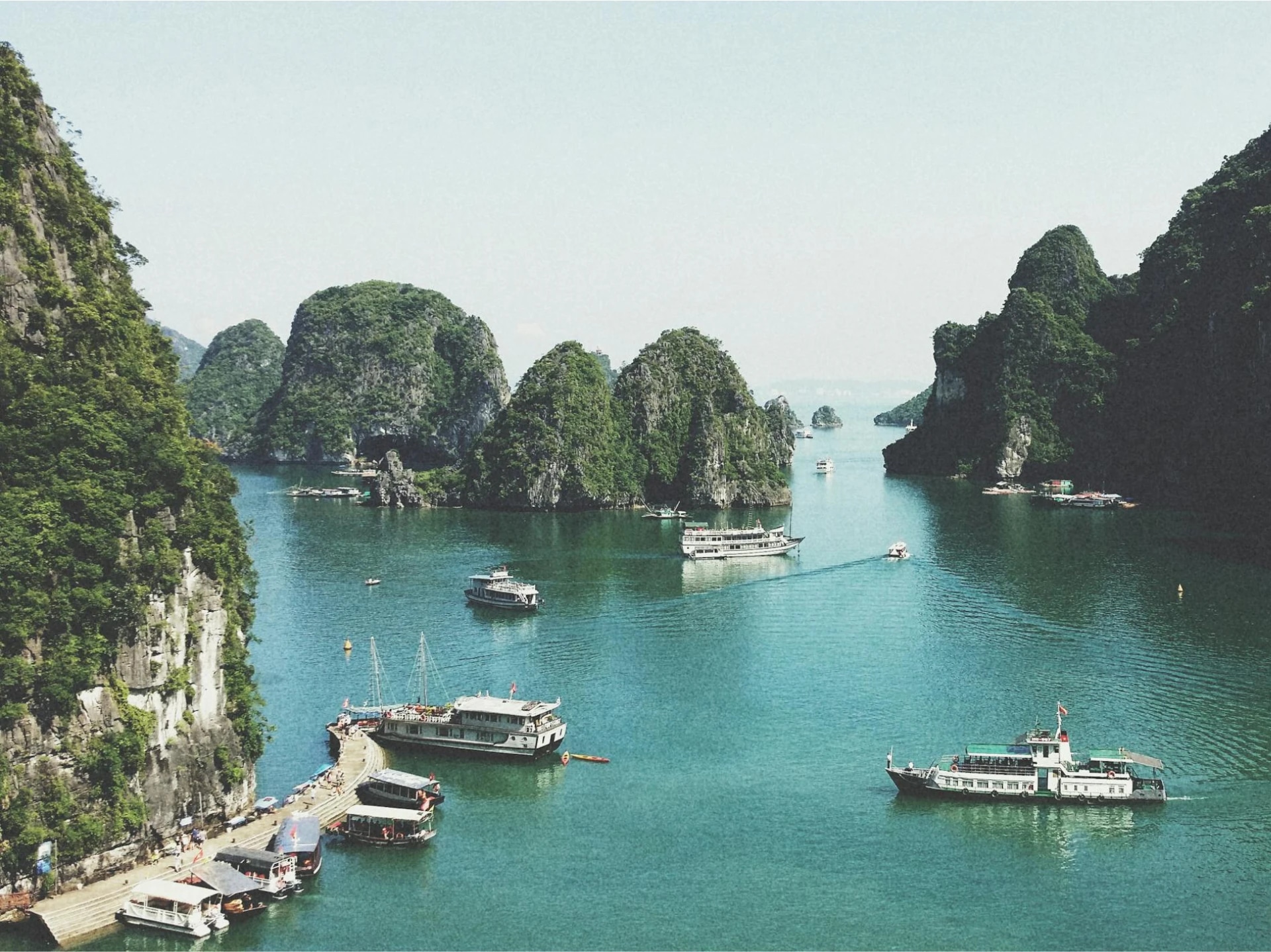 Scenic view of emerald waters with multiple boats and lush green limestone islands.