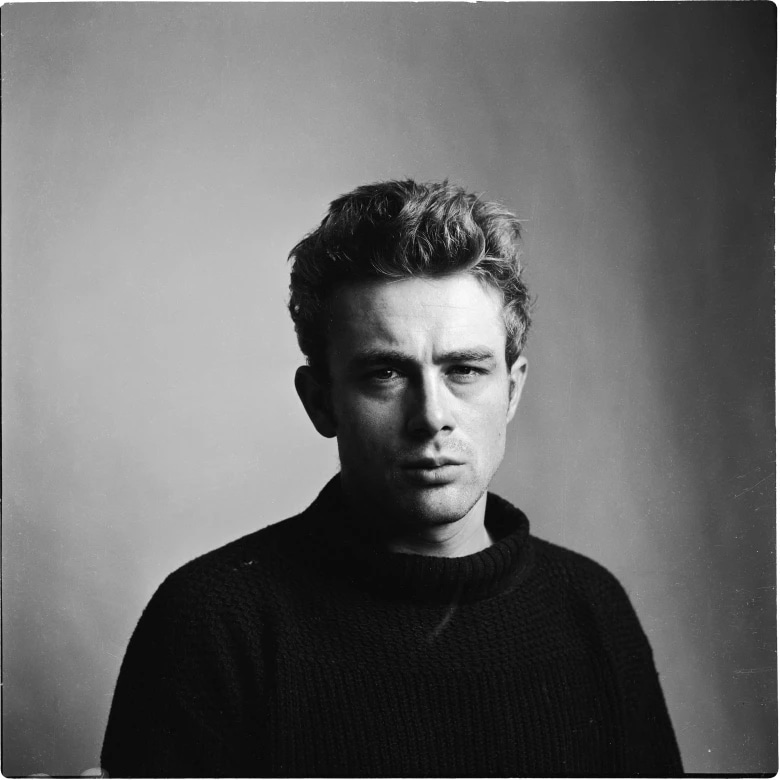 Black and white portrait of a young man with wavy hair wearing a dark sweater, looking directly at the camera.