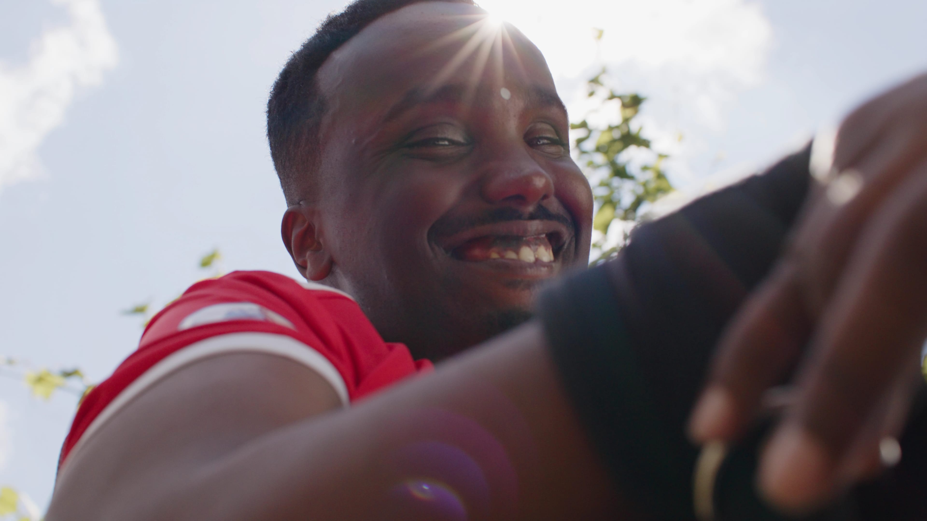 Man looking down and smiling into the camera, the sun shines behind him
